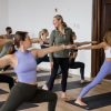 Lisa Bermudez of YogaRenew leading a yoga class in a forest green zip up with all her students in Warrior 2 pose surrounding her.